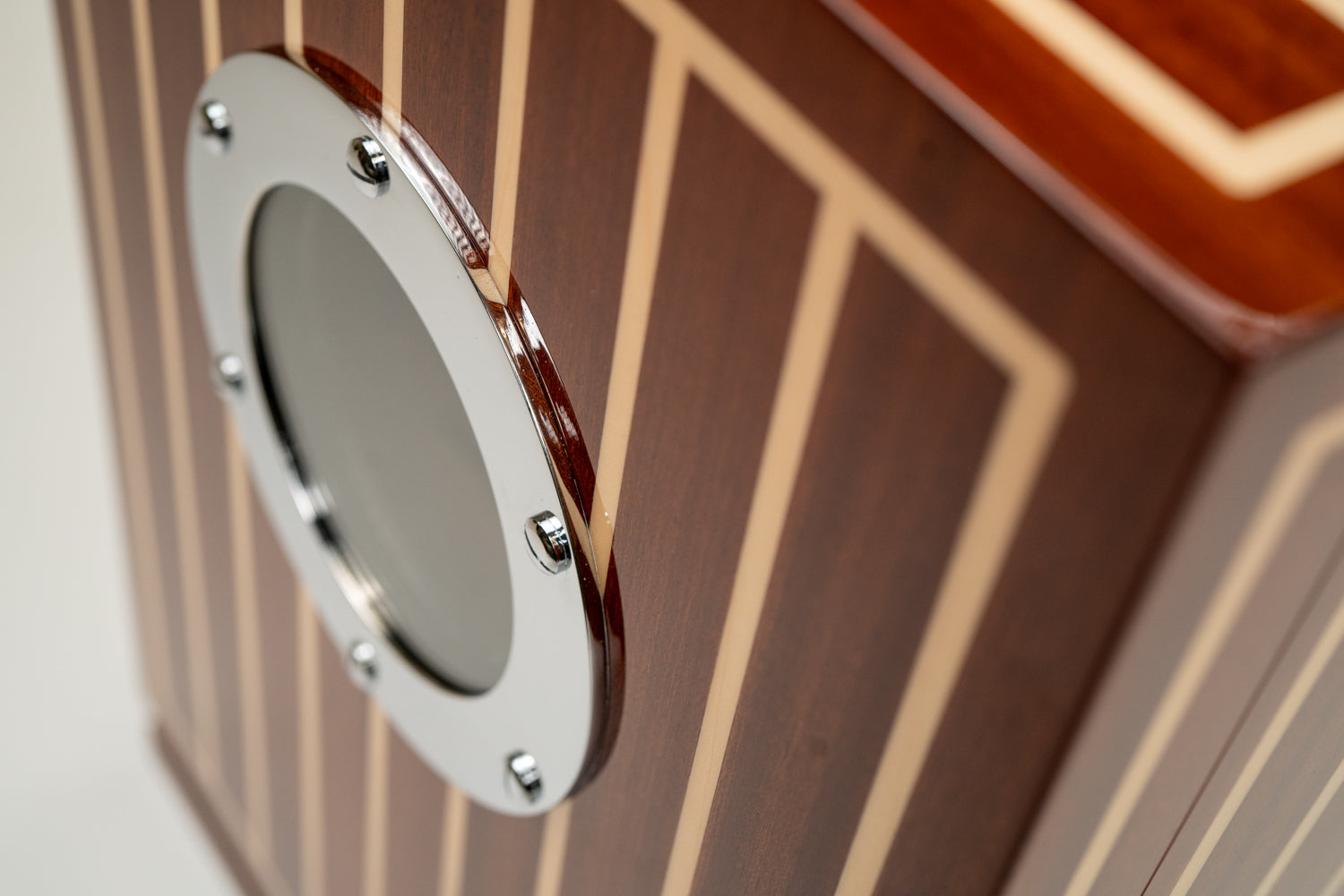 Close-up of a glossy cigar humidor inlaid with mahogany and maple pinstripes like a classic boat deck, with a polished chrome porthole window on its front.