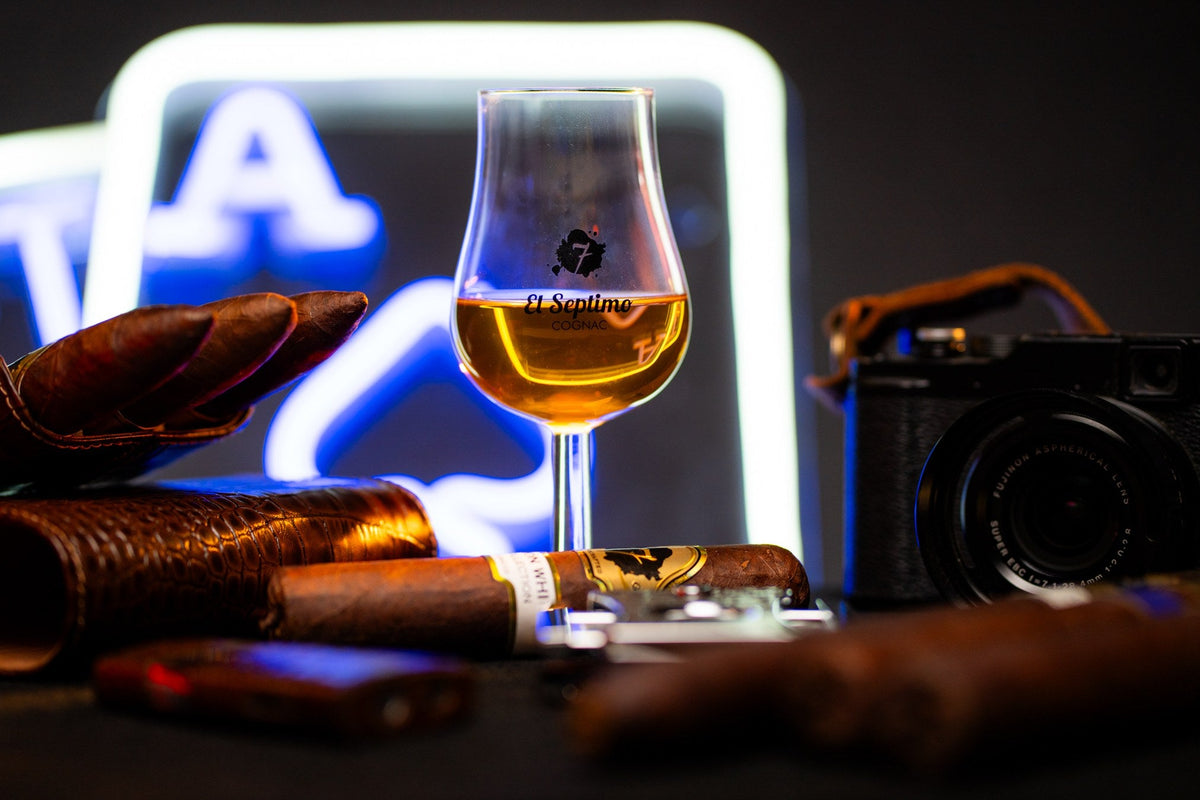 Premium cigars, a cigar cutter and a tasting glass of cognac on a dark table
