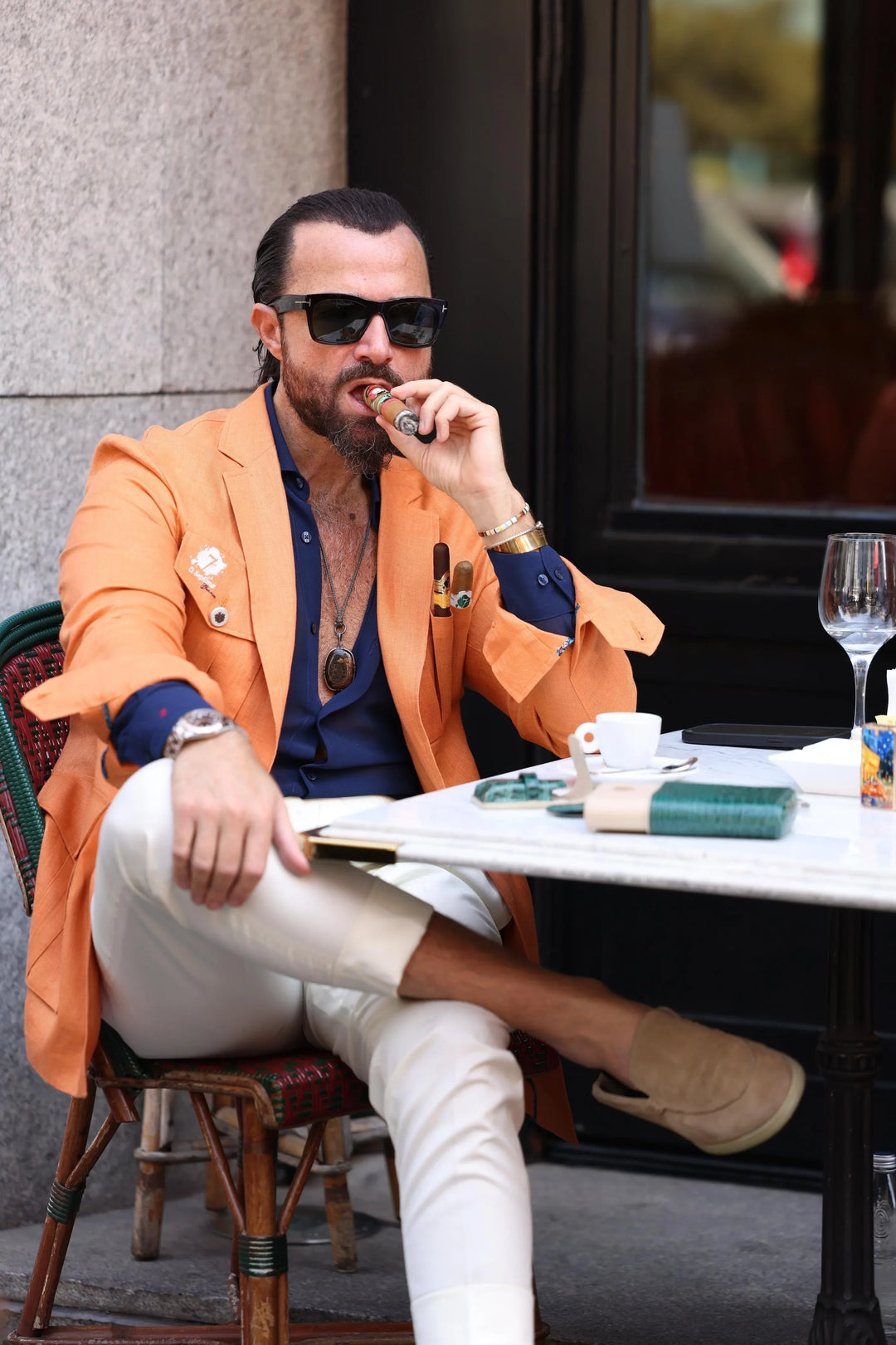 Man sitting outside at a restaurant smoking a premium cigar and wearing an orange El Septimo Smoking Suit Jacket with 3 cigar pockets available at Cigar Inc in Woodland Hills