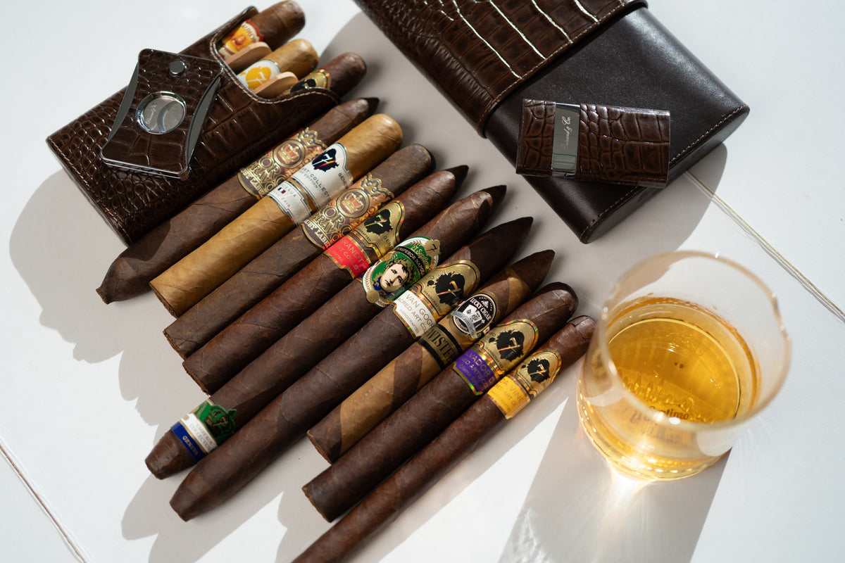Row of premium cigars with a leather cigar case, cutter and a glass of whiskey for a groomsmen gift